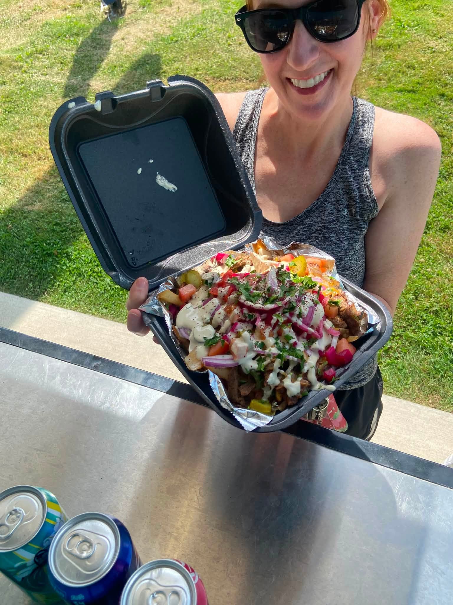 A customer holding a box of loaded shawarma fries with tahini, pickled turnips and parsley